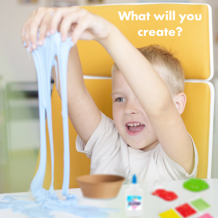 A young boy with blond hair sits in a yellow chair, smiling as he stretches light blue slime with both hands. A white text overlay reads 'What will you create?'.