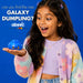 A young girl with long dark hair holds a small blue glittery dumpling toy in her hand, looking excited. She is wearing a pastel multicolor knit cardigan over a light purple crop top, set against a solid blue background with promotional text that reads 'can you find the rare GALAXY DUMPLING?' and the brand name 'abeec'.