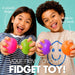 Two children smiling and holding colorful fidget toys against a light blue background, with promotional text reading '4 colourful designs', 'Made for busy hands', and 'your new favourite FIDGET TOY!'.