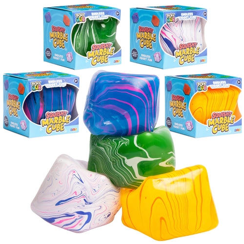 Four colourful squishy marble cubes displayed in front of their blue retail boxes on a white background. The cubes feature marbled swirl patterns in blue, green, yellow, pink, and purple, with some showing smooth solid colors.