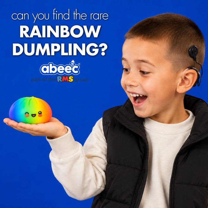A young boy wearing a black puffer vest over a white shirt holds a small, round, rainbow-colored dumpling toy with a cute face. He has a small black device attached to his ear, and the background is a solid blue with text reading 'can you find the rare RAINBOW DUMBLING?' and the 'abeec' brand logo.
