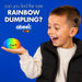 A young boy wearing a black puffer vest over a white shirt holds a small, round, rainbow-colored dumpling toy with a cute face. He has a small black device attached to his ear, and the background is a solid blue with text reading 'can you find the rare RAINBOW DUMBLING?' and the 'abeec' brand logo.