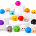 A collection of colourful, cute dumpling-shaped stress balls with smiling faces, displayed on white geometric risers against a white background.
