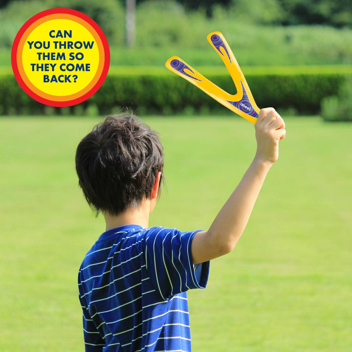 Child holding a yellow and blue boomerang with text asking if it can be thrown to come back, set against a grassy outdoor background.